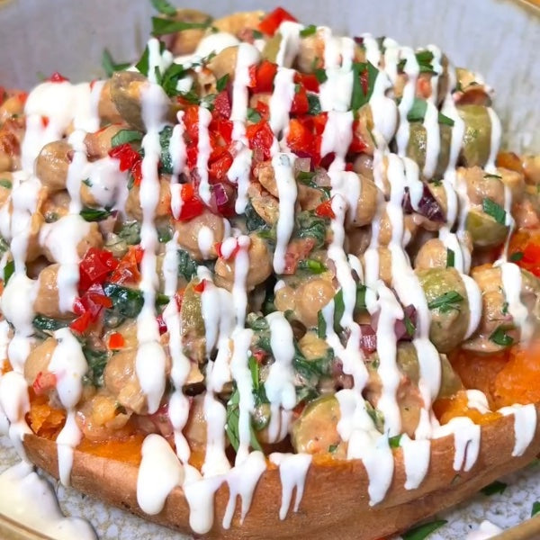 Stuffed sweet potato with chickpeas and tahini sauce, a healthy vegan recipe from Vegan Fndly, topped with fresh herbs and ingredients.