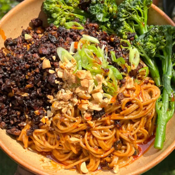 Vegan Fndly Tofu Dan Dan Noodles recipe with bowls of noodles, tofu, and spicy sauce on a wooden table.